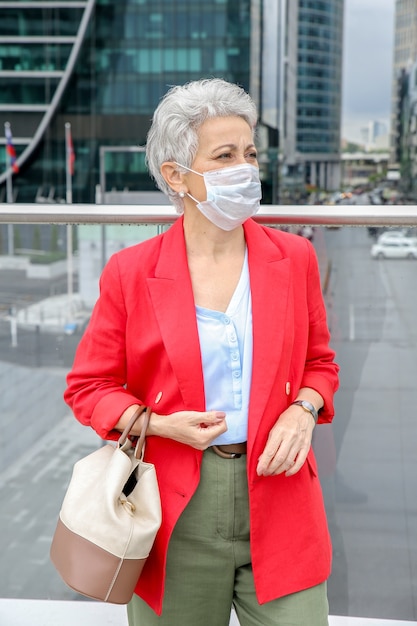 Elegante grauhaarige Frau auf der Straße in einer medizinischen Maske