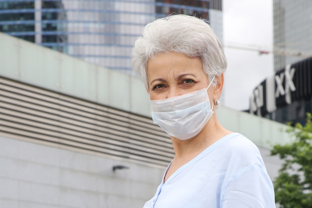 Elegante grauhaarige Frau auf der Straße in einer medizinischen Maske