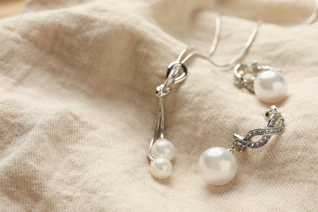 Elegante Halskette und silberne Ohrringe mit Perlen auf beiger Stoffnahaufnahme