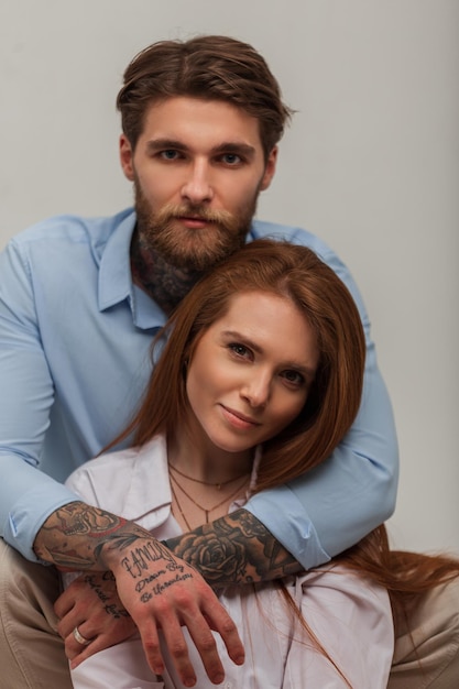 Elegante hermosa joven pareja de moda Pelirroja hermosa chica y moda guapo hipster brutal chico con un tatuaje y una barba en una camisa