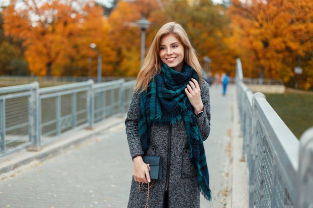 Elegante hermosa mujer feliz con una sonrisa en un abrigo de moda con una bufanda y un bolso en un día de otoño