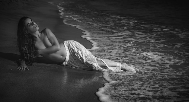 Elegante hermosa mujer morena con falda larga blanca en la playa en españa