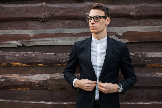 Elegante, hermoso, hombre en traje clásico, posando junto a la pared de madera.