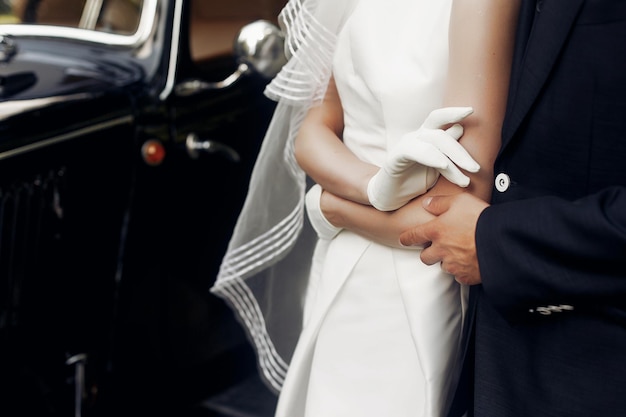 Elegante, hinreißende Braut und stilvoller, gutaussehender Bräutigam, die Händchen halten, Nahaufnahme, sanfte Berührung, ungewöhnliche Luxushochzeit im Retro-Stil, erstaunlicher romantischer Moment