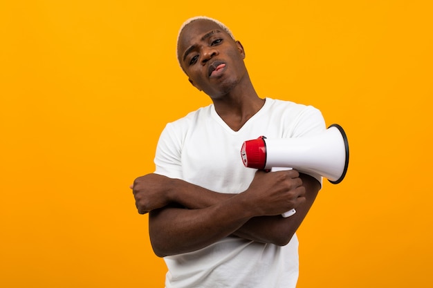 Elegante hombre americano negro guapo en camiseta blanca con un megáfono sobre fondo naranja aislado