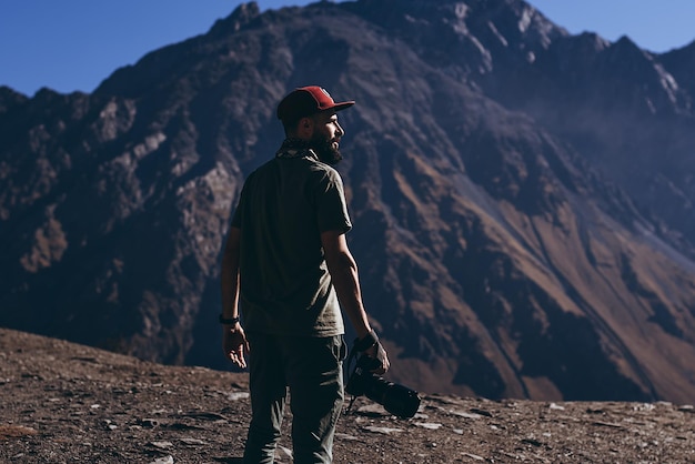 Elegante hombre barbudo con cámara en la parte superior de las montañas georgianas viajero fotógrafo de naturaleza