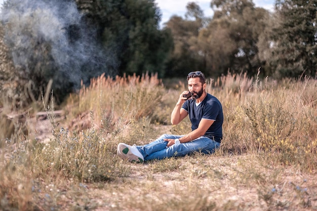 Foto elegante hombre barbudo fuma cigarrillo electrónico exhala humo. hombre guapo.