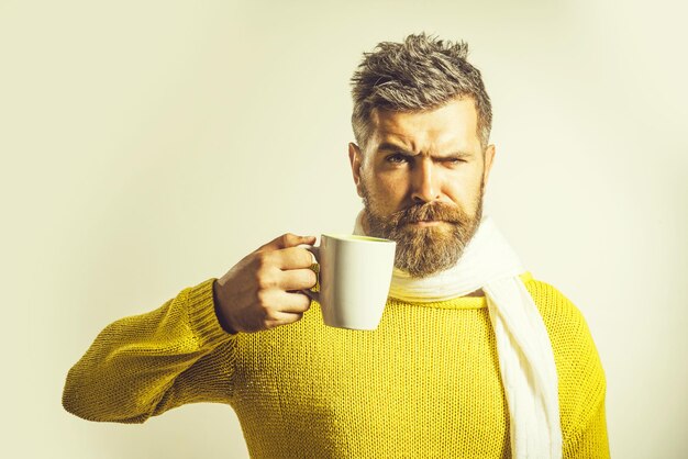 Elegante hombre barbudo guapo en bufanda y suéter sostiene la taza con publicidad de té o café caliente para