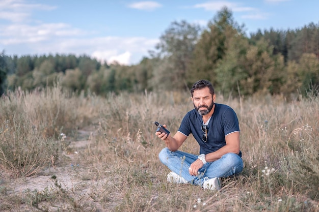 El elegante hombre brutalvape hace estallar a una pareja un dispositivo electrónico de humo en el bosque. concepto de salud.