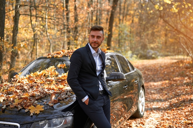 Elegante hombre caucásico traje blanco cerca del coche Temporada de otoño