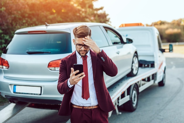 Elegante hombre de negocios de mediana edad llamando al servicio de remolque para pedir ayuda en la carretera. Concepto de asistencia en carretera.