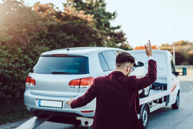 Elegante hombre de negocios de mediana edad con servicio de remolque para ayudar a accidentes automovilísticos en la carretera. Concepto de asistencia en carretera.