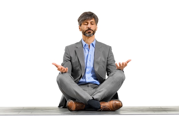 Elegante hombre de negocios meditando en la postura del loto de yoga sentado en una colchoneta de ejercicios con los ojos cerrados y la expresión serena aislada