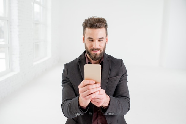 Elegante hombre de negocios en traje oscuro con teléfono en el interior de la oficina blanca