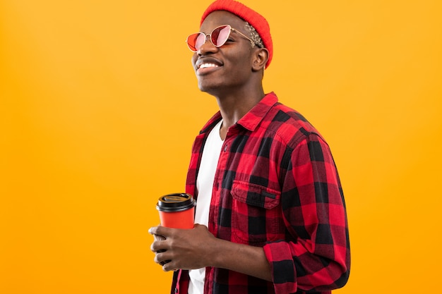 Elegante hombre negro americano en camisa roja a cuadros con vaso de café en amarillo