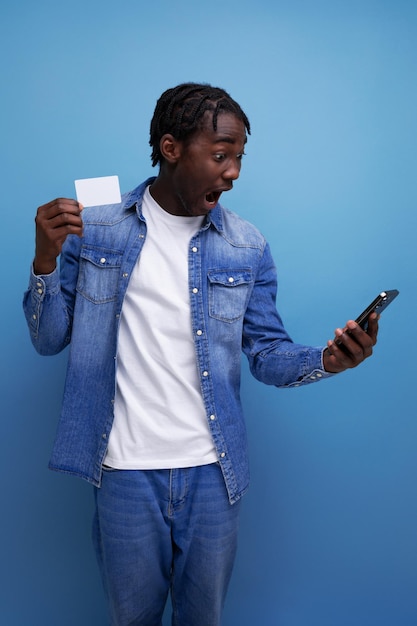 Elegante homem americano com dreadlocks pretos segurando maquete de cartão de dinheiro e smartphone