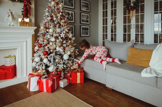 Elegante interior de natal com um sofá elegante conforto em casa presentes e presentes embrulhados sob a árvore de natal com luz e bugiganga na ensolarada sala de estar árvore de natal com presentes