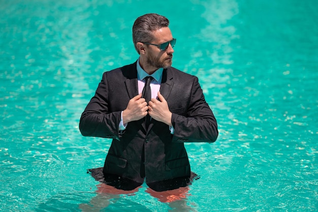 Elegante jefe de negocios en la piscina de verano con foto de traje del jefe de negocios relajarse en la piscina de verano