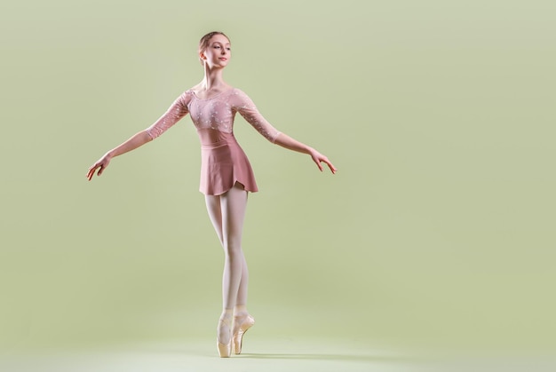 Elegante jovem bailarina em sapatilhas dançando sobre um fundo verde suave