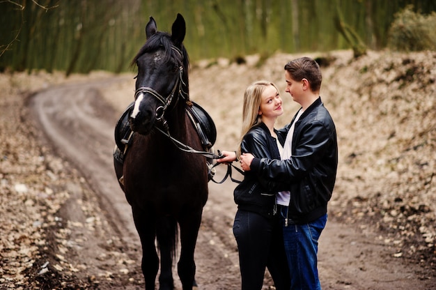 Elegante jovem casal apaixonado perto de cavalo na floresta de outono