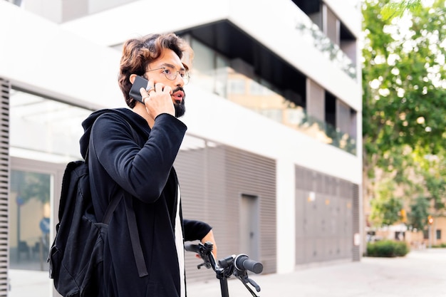 Elegante jovem com uma bicicleta falando em seu telefone