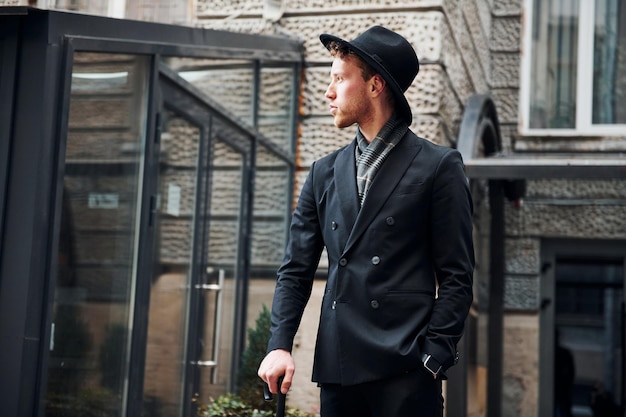 Elegante jovem de chapéu preto e roupas com guarda-chuva nas mãos ao ar livre na cidade