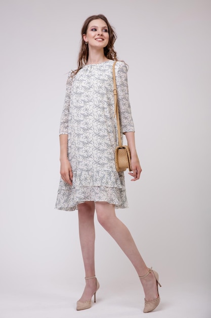 Elegante jovem de vestido bege bonito com padrão floral, bolsa posando em fundo branco