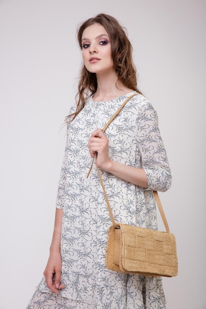 Elegante jovem de vestido bege bonito com padrão floral, bolsa posando em fundo branco