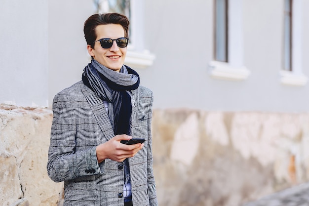 Elegante jovem em óculos de sol com telefone na rua