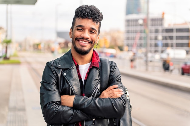 Elegante jovem empresário latino sorrindo feliz olhando para a câmera com os braços cruzados, conceito de estilo de vida urbano