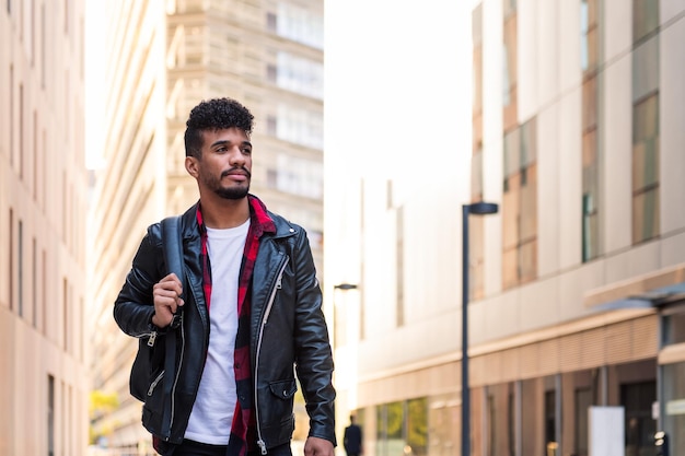 Elegante jovem estudante latino caminhando pela cidade com sua mochila, conceito de estilo de vida urbano