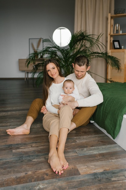 Elegante jovem família com um bebê está sentado no chão do quarto e desfrutando de momentos felizes