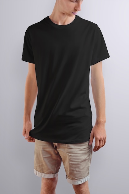 Elegante jovem homem caucasiano em uma camiseta preta e shorts marrom de algodão em um fundo branco do estúdio. Pose frontal. O modelo pode ser usado em seu design.