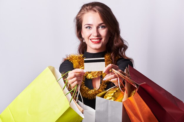 Elegante jovem morena segurando sacolas coloridas e cartão de crédito