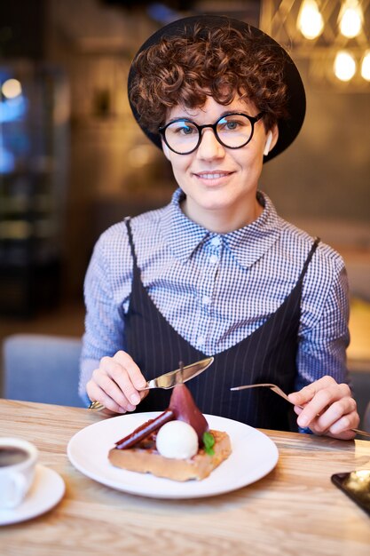 Elegante jovem morena sentada à mesa no café e vai comer sobremesa de frutas