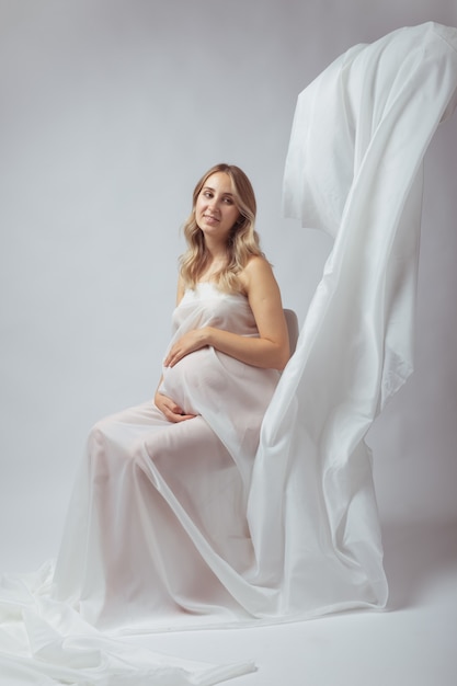 Elegante joven embarazada de pie vistiendo tela blanca voladora embarazo maternidad y maternidad