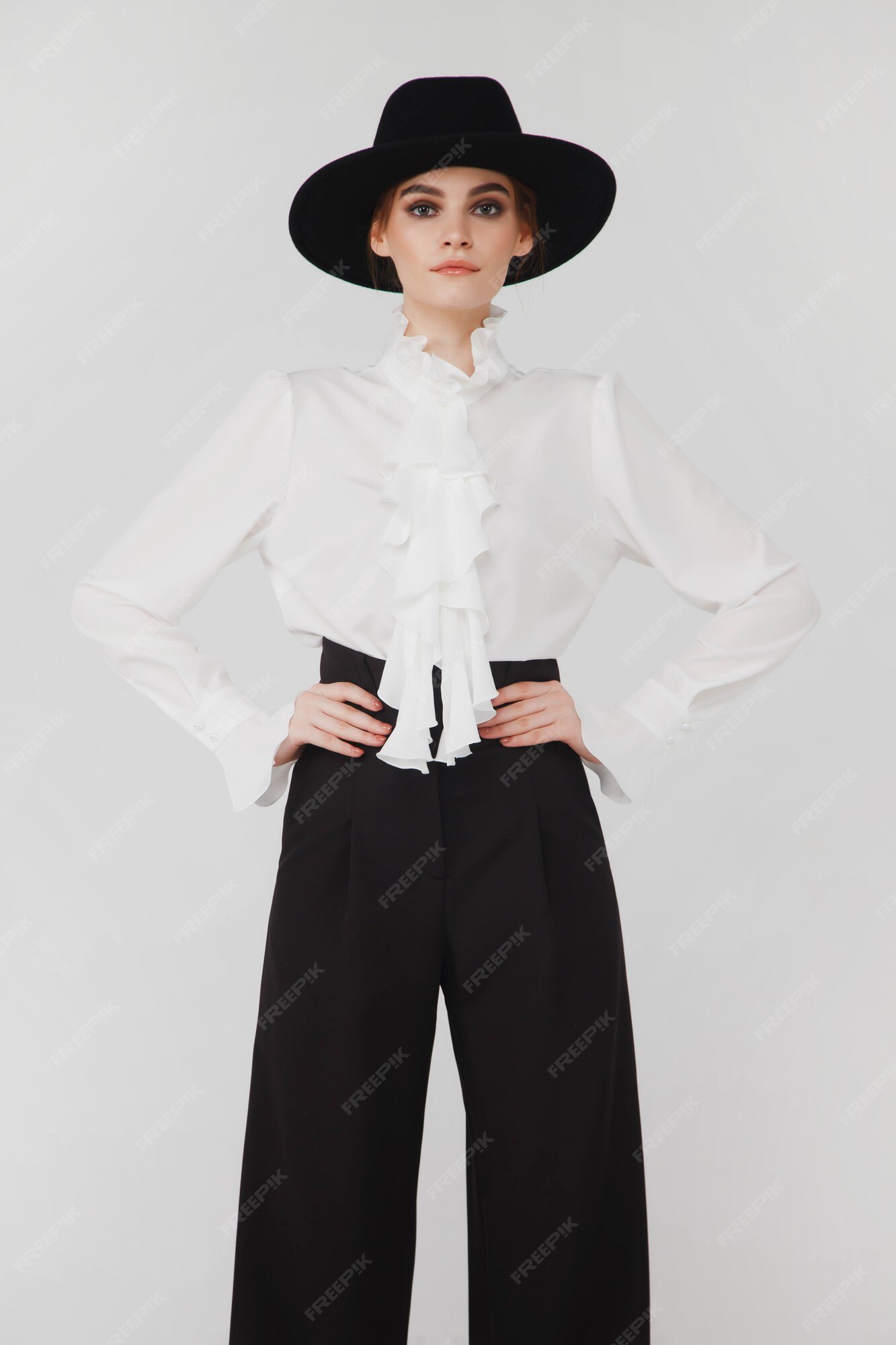 Elegante empresaria linda en elegante blusa blanca y sombrero sobre fondo blanco claro. mujer en ropa de moda posando la cámara. concepto de estilo, moda, y consecución de objetivos