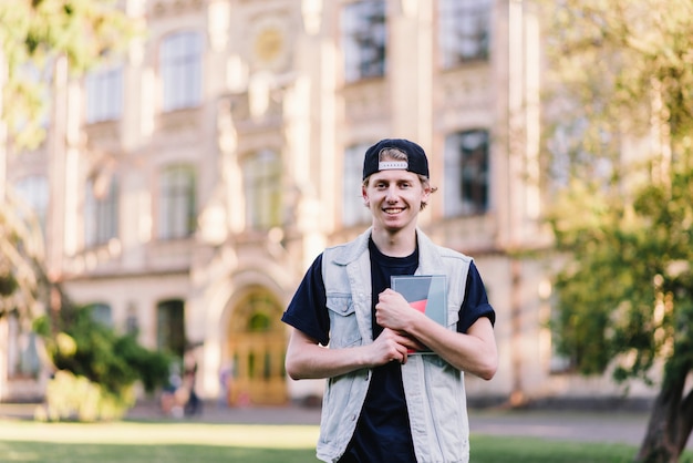 Elegante joven estudiante con gorra cerca de la universidad