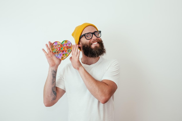 Elegante joven hipster alegre con barba juega con un popular juguete pop it Antiestrés sensorial fidget push pop toy