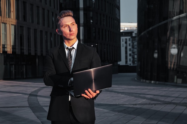 Elegante joven hombre de negocios con laptop por la noche al atardecer después del trabajo. Banquero de hombre de negocios masculino relajado en la oficina de fondo ubicada en el distrito financiero. copia espacio