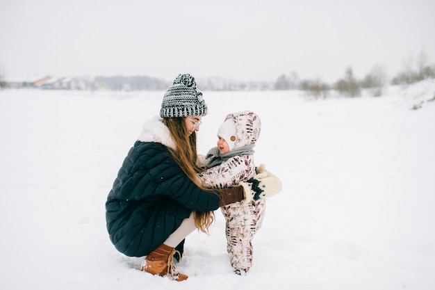 Elegante joven madre jugando con bebé en la naturaleza en invierno