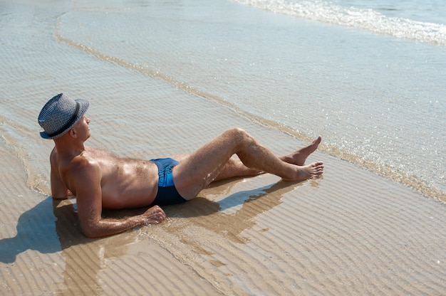 Elegante joven modelo masculino hombre tumbado en la arena de la playa