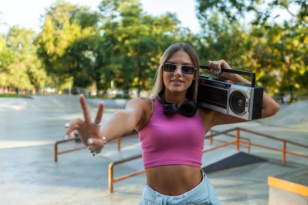 Elegante joven mujer rubia en top rosa con grabadora de casete boombox retro de los años 80 al aire libre