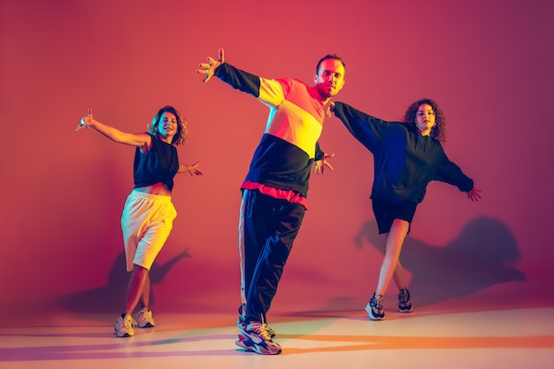 Elegante joven y mujeres bailando hip-hop en ropa brillante sobre fondo degradado en el salón de baile con luz de neón. Cultura juvenil, movimiento, estilo y moda, acción, hip-hop. Retrato de moda.