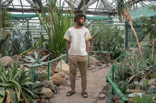 Elegante joven de pie en el invernadero con plantas tropicales