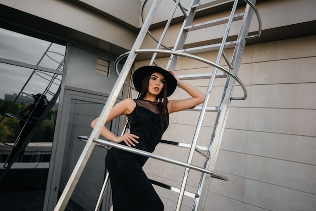 Elegante joven posando en un sombrero en la escalera de incendios del centro de negocios. Moda.