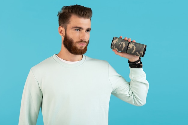 Foto elegante joven sonriente sosteniendo altavoz inalámbrico escuchando música estilo colorido feliz estado de ánimo aislado sobre fondo azul.