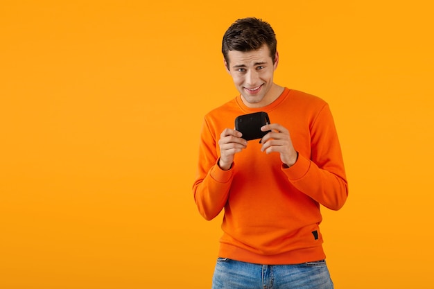 Elegante joven sonriente en suéter naranja con altavoz inalámbrico feliz escuchando música divirtiéndose