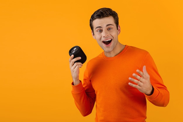 Elegante joven sonriente en suéter naranja con altavoz inalámbrico feliz escuchando música