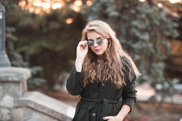 Elegante jovencita vistiendo chaqueta de invierno y gafas de sol al aire libre